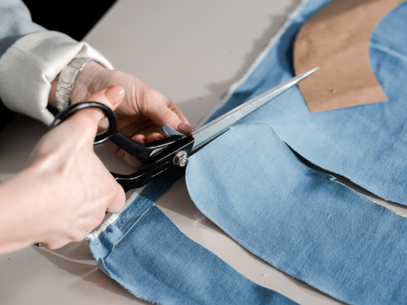A person cutting out some blue fabric from a paper pattern